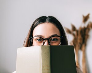 Frau mit Brille hält sich ein grünes Buch vor das Gesicht